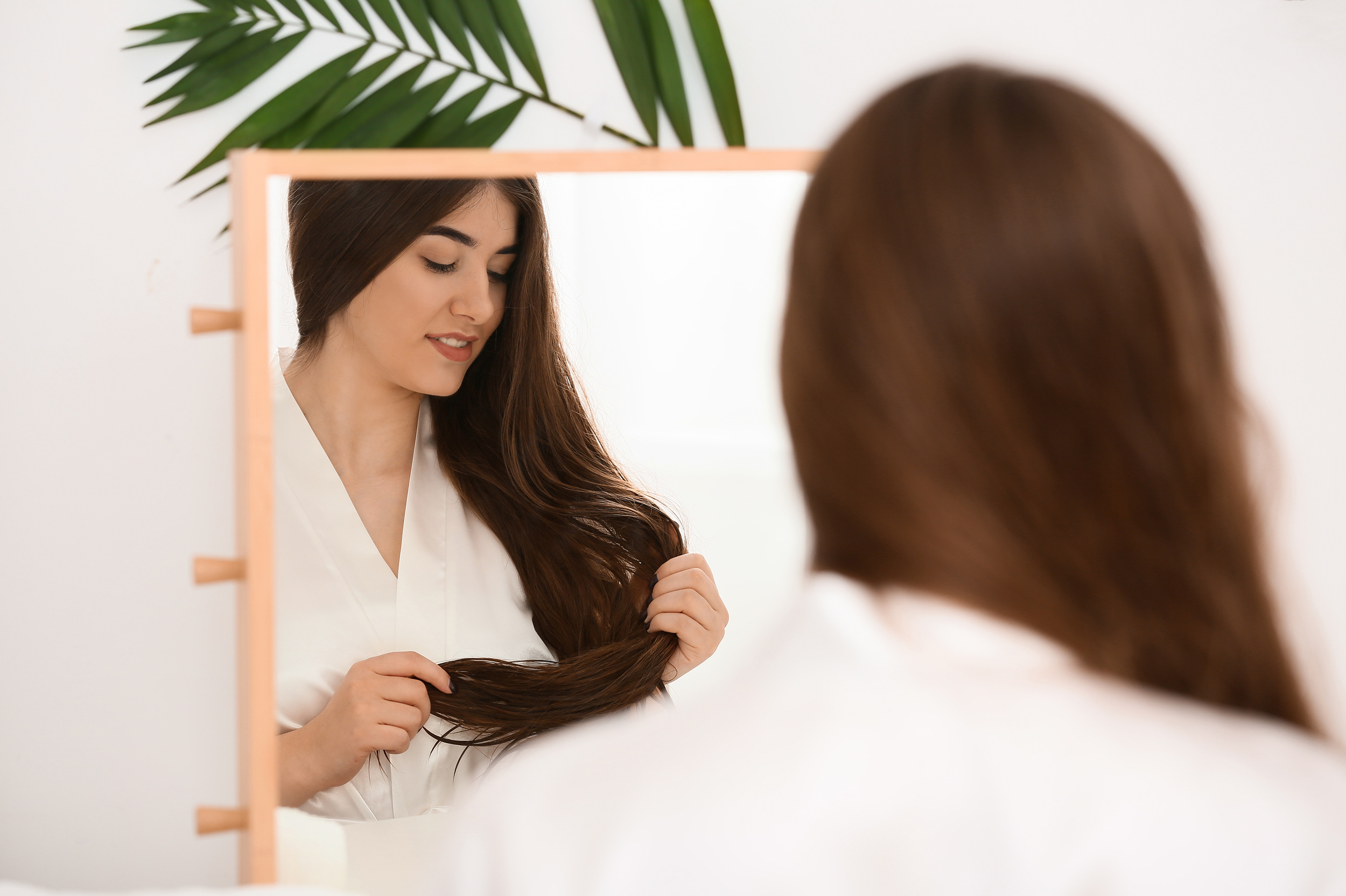 Ruskeahiuksinen nainen peilaa itseään peilistä ja harjaa hiuksiaan